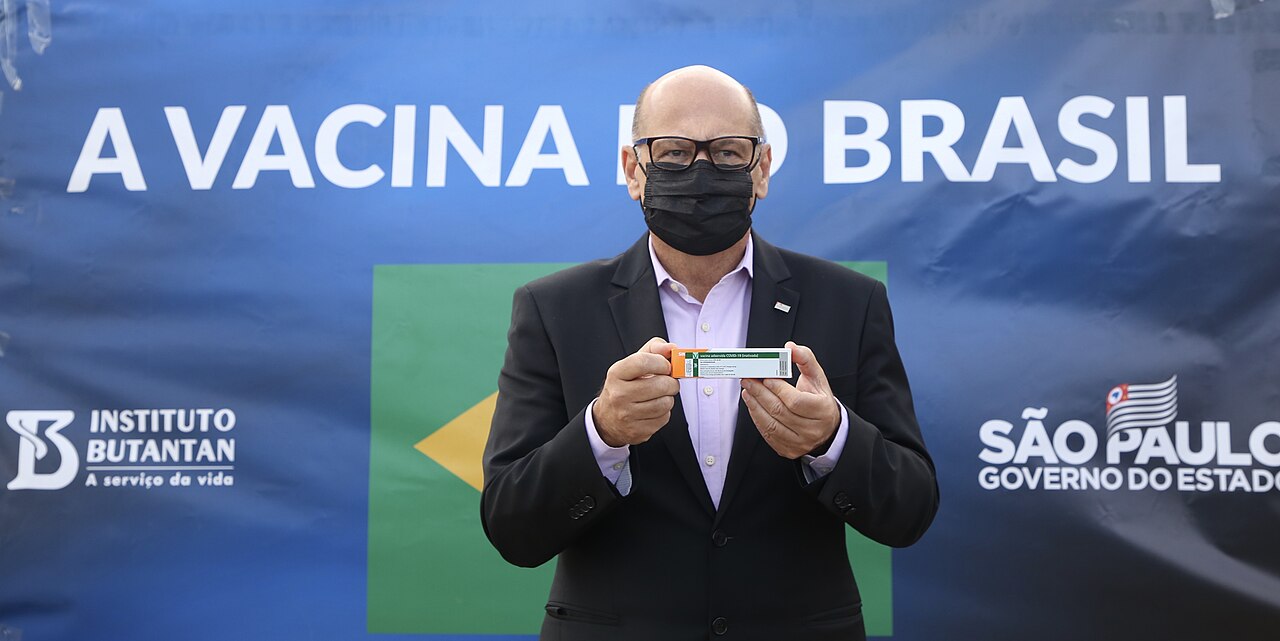 Dimas Covas exibe frasco da CoronaVac diante do painel 'A vacina do Brasil', na chegada de lote de 5,5 milhões de doses a São Paulo em 24/12/2020 — doses já estocadas sem contrato federal.